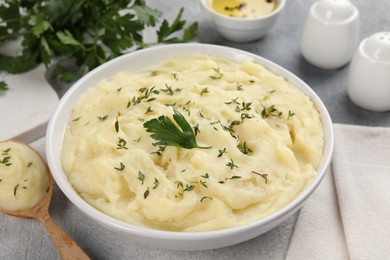 Photo of Bowl of tasty mashed potato, parsley, olive oil and pepper on grey marble table, closeup