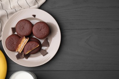 Photo of Tasty banana choco pies and pieces of chocolate on grey wooden table, flat lay. Space for text