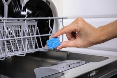 Photo of Woman putting detergent tablet into open dishwasher in kitchen, closeup