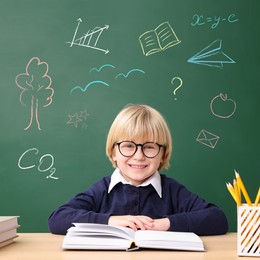 Image of School boy at desk near green chalkboard with drawings and inscriptions