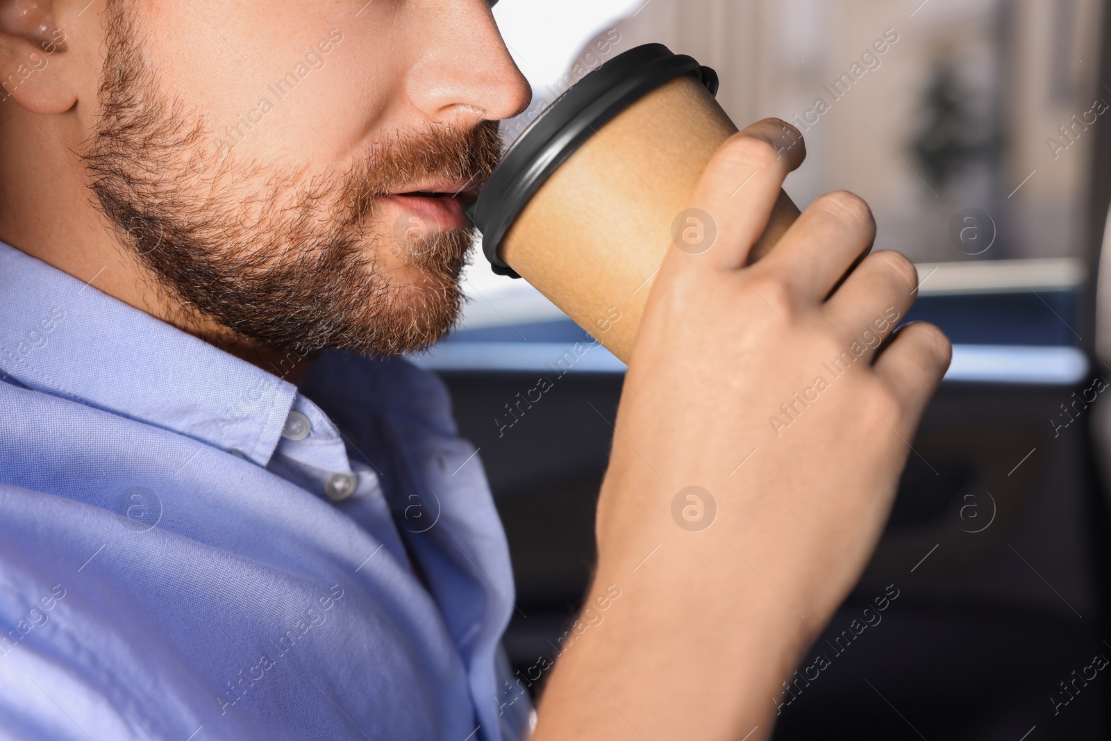 Photo of To-go drink. Man drinking coffee in car, closeup