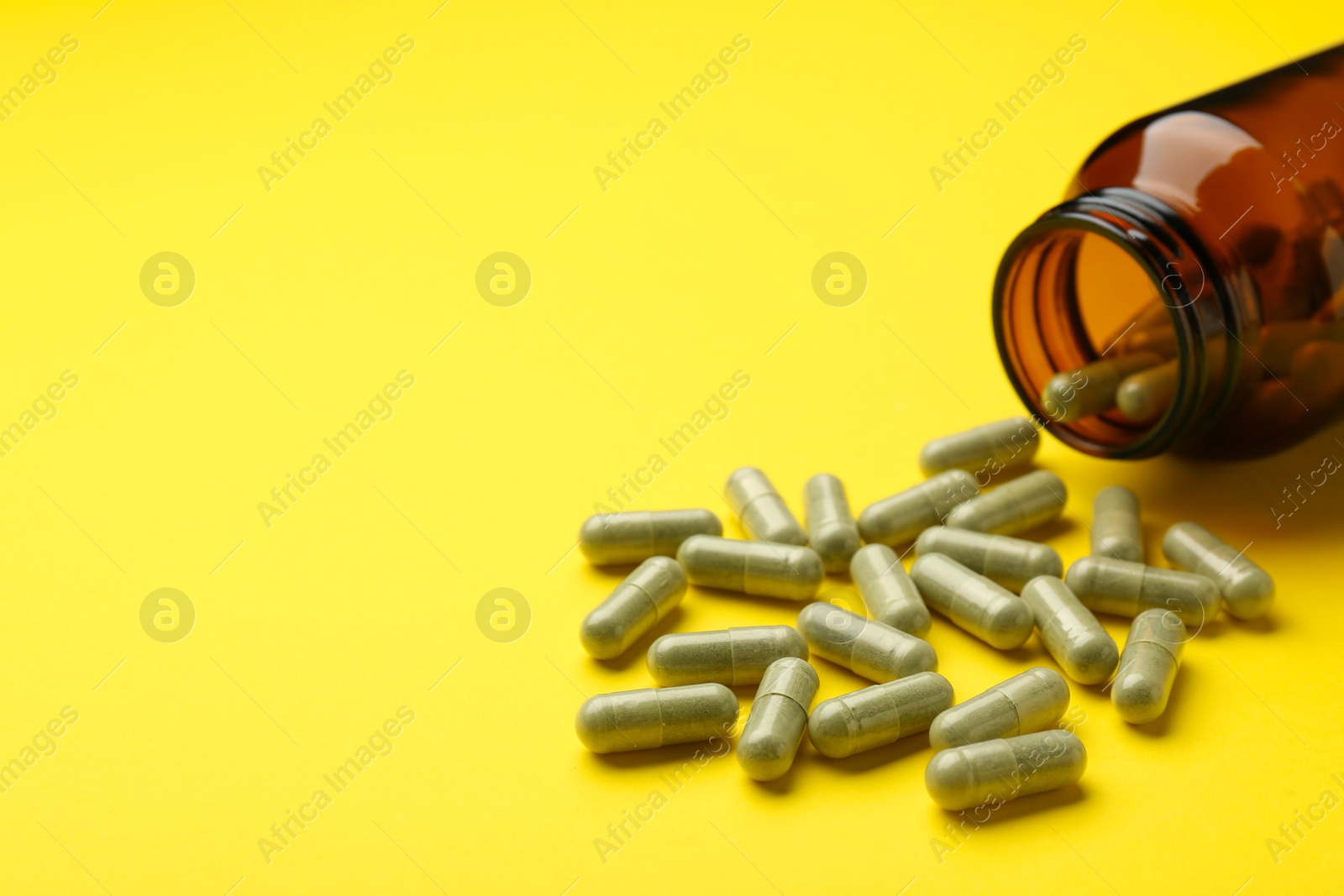 Photo of Vitamin pills and bottle on yellow background, closeup. Space for text