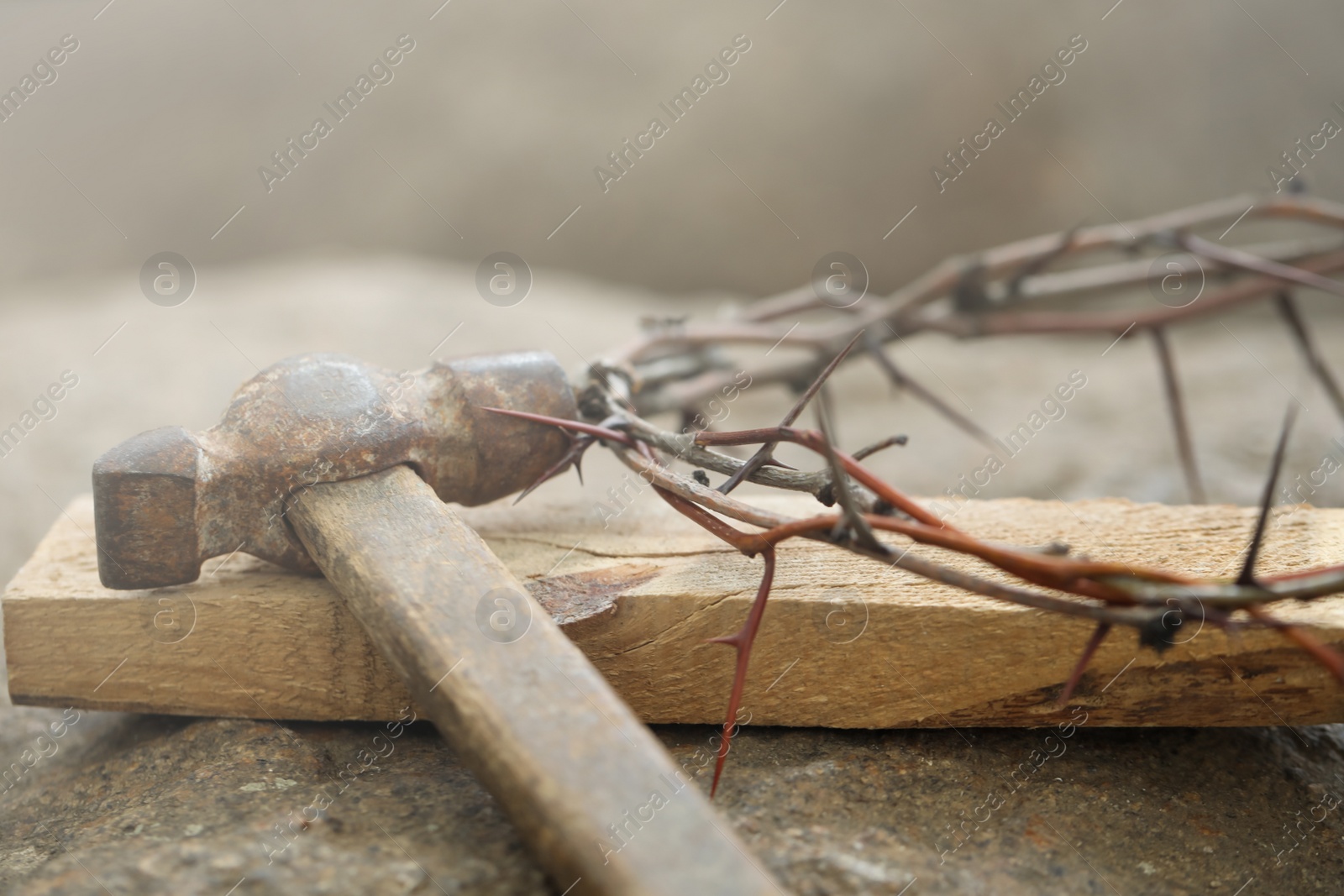 Photo of Crown of thorns, wooden plank and hammer on stone, closeup. Easter attributes