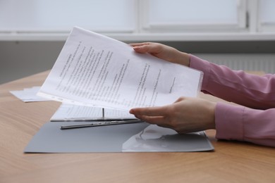 Photo of Woman putting punched pocket with document into folder at wooden table, closeup