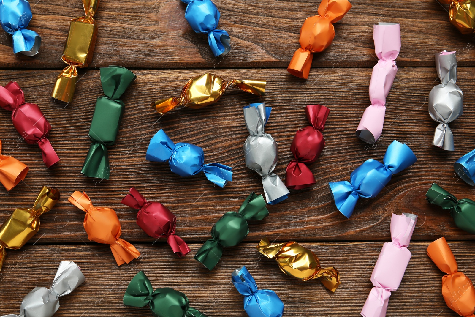 Photo of Many candies in colorful wrappers on wooden table, flat lay