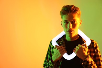Photo of Young man with square lamp on color background in neon lights. Space for text