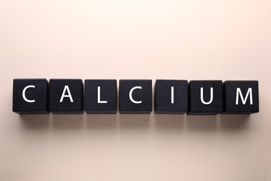 Word Calcium made of black wooden cubes with letters on beige background, flat lay