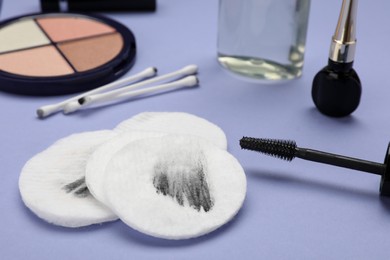 Photo of Dirty cotton pads after removing makeup, swabs and cosmetic products on violet background, closeup