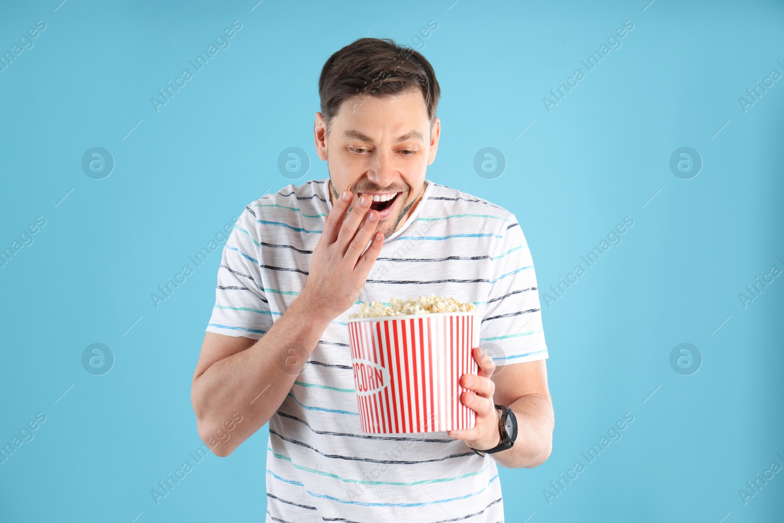 Photo of Emotional man with tasty popcorn on color background