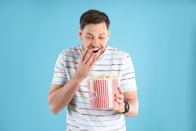 Emotional man with tasty popcorn on color background