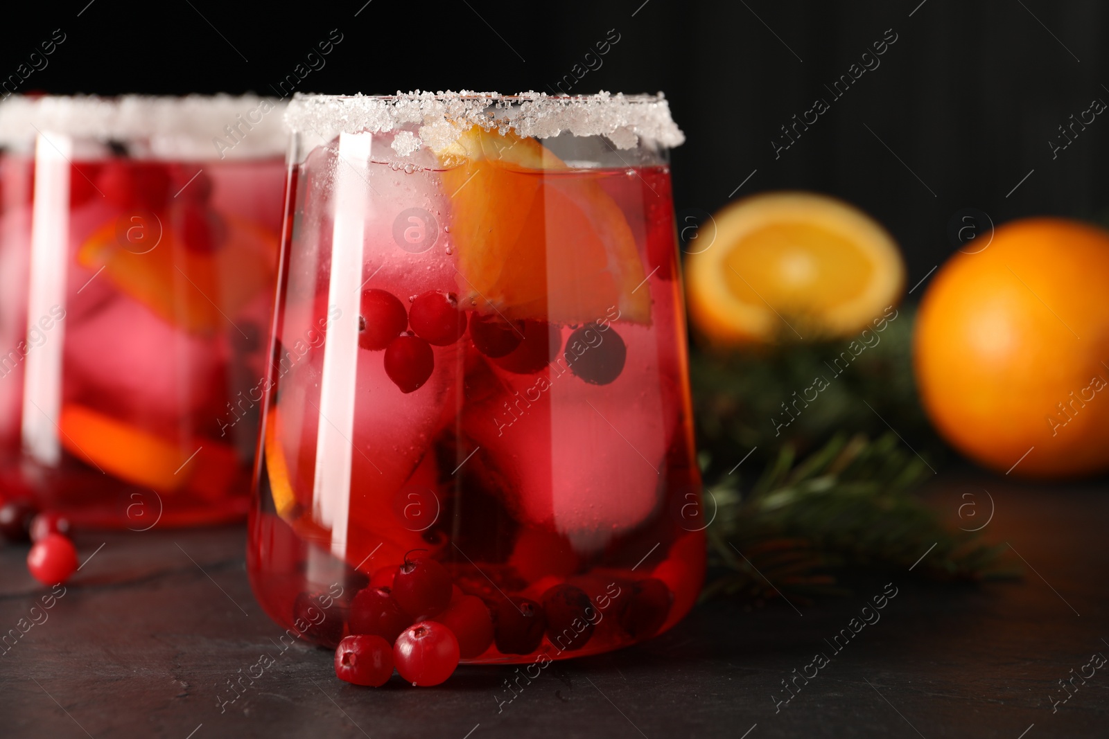 Photo of Tasty cranberry cocktail with ice cubes in glasses on dark gray table, closeup
