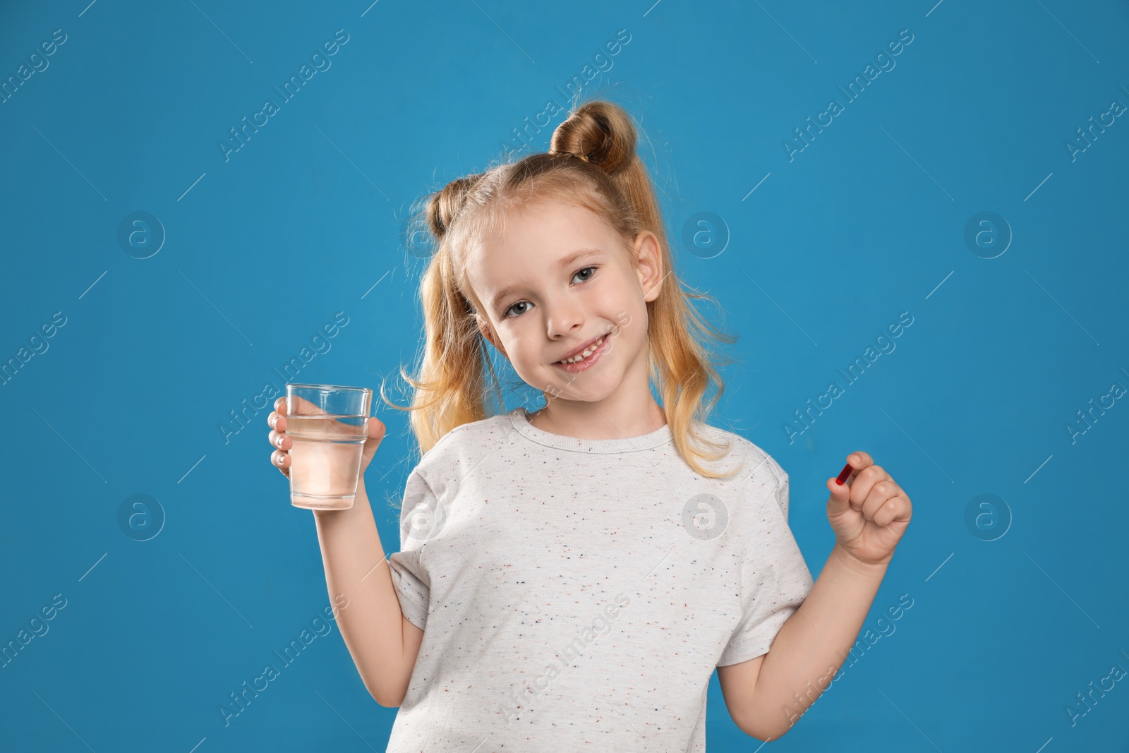 Photo of Little girl with vitamin pill and glass of water on blue background