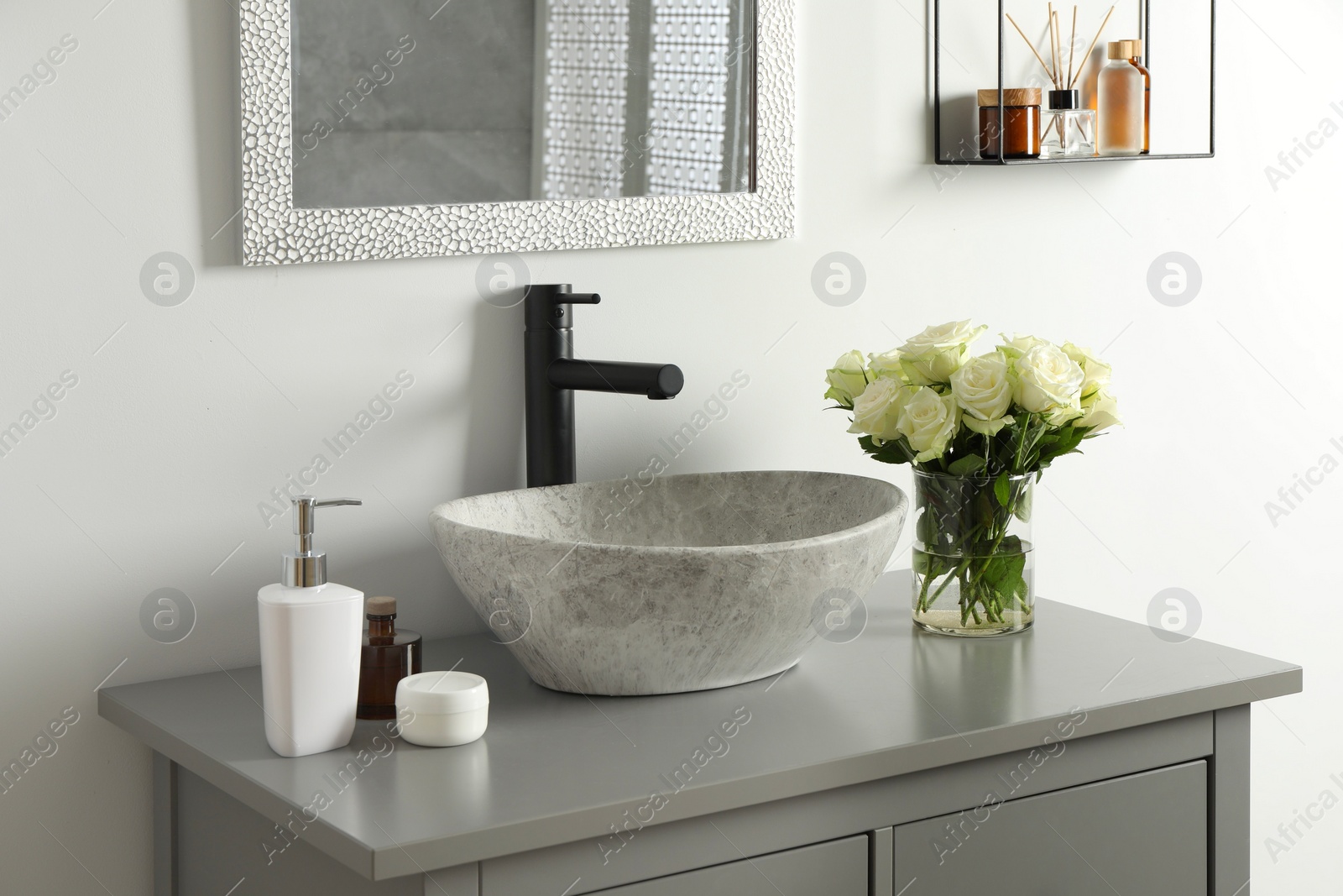 Photo of Vase with beautiful white roses and toiletries near sink in bathroom