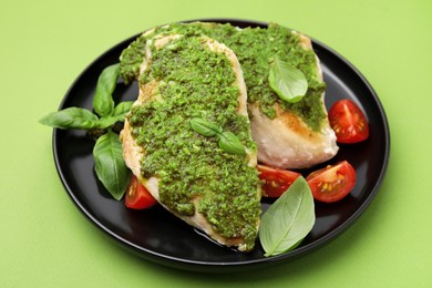 Photo of Delicious chicken breasts with pesto sauce, tomatoes and basil on light green table, closeup