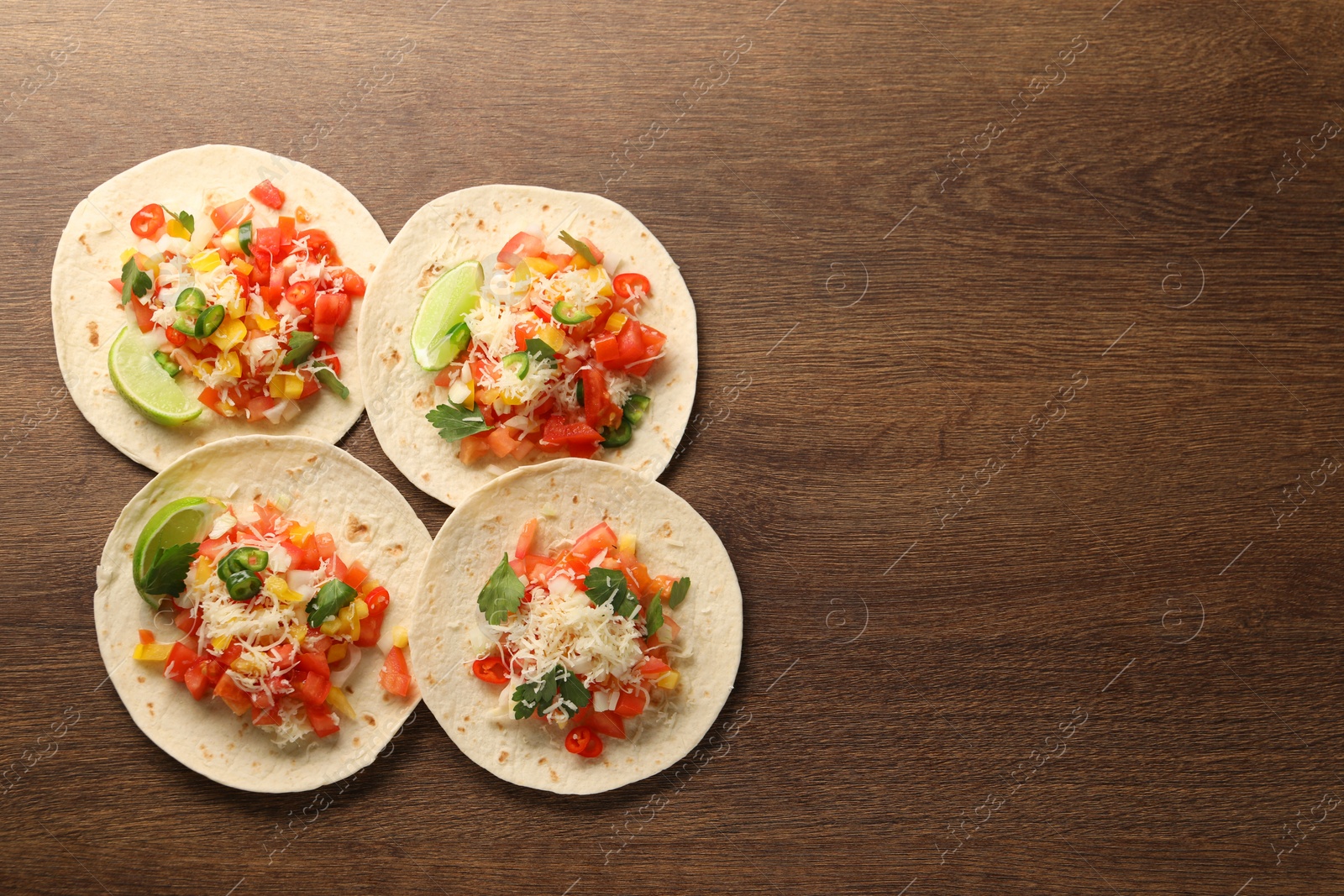 Photo of Delicious tacos with vegetables and lime on wooden table, top view. Space for text