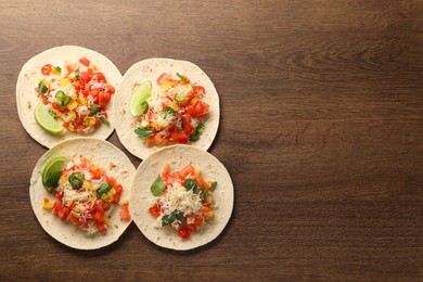 Delicious tacos with vegetables and lime on wooden table, top view. Space for text