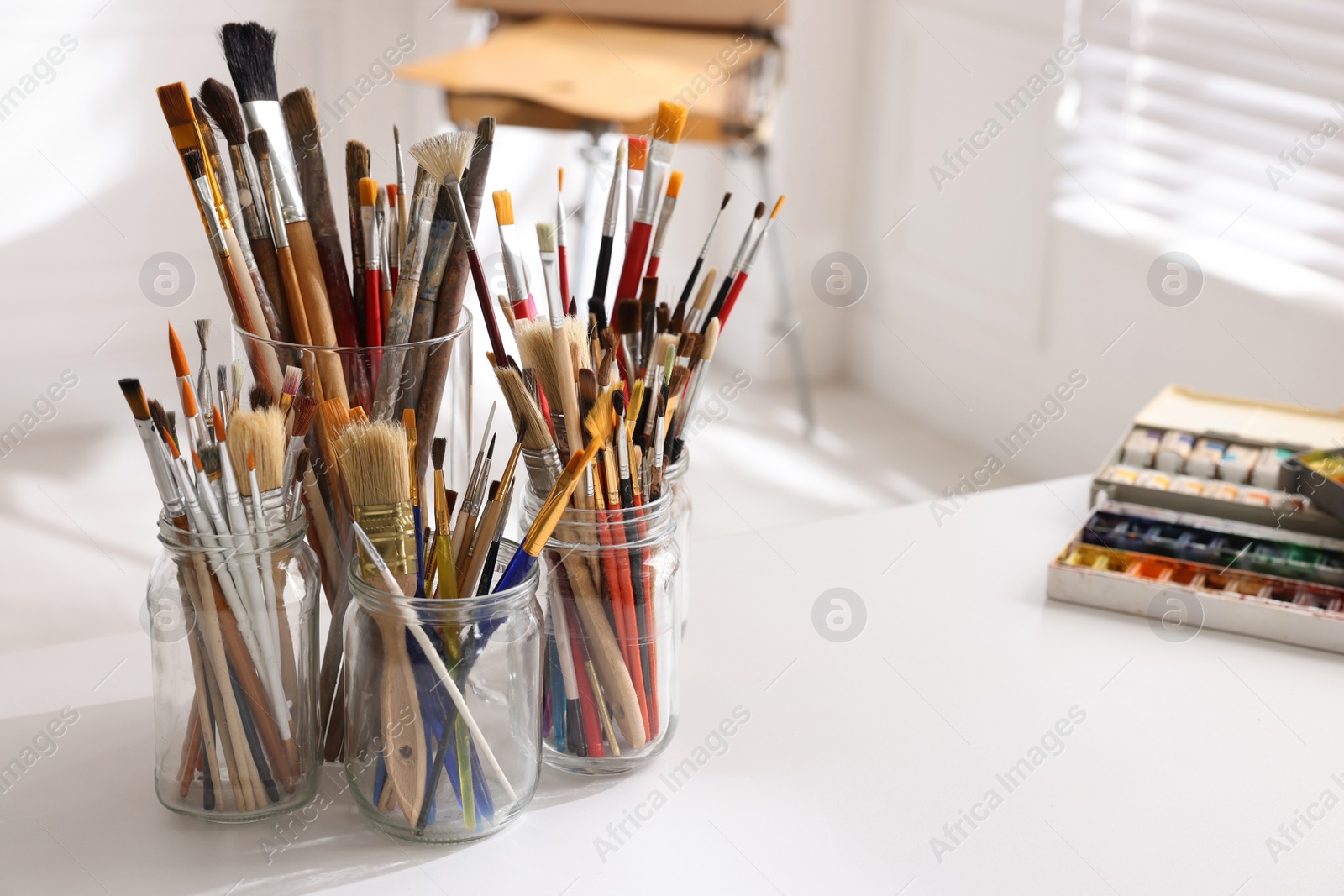 Photo of Different brushes and paints on white table in studio, space for text. Artist's workplace