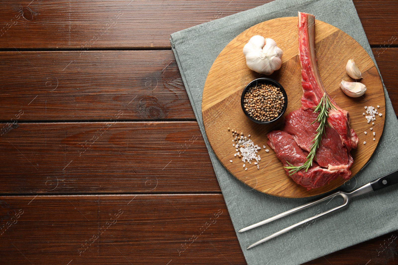 Photo of Raw ribeye steak, spices and fork on wooden table, flat lay. Space for text