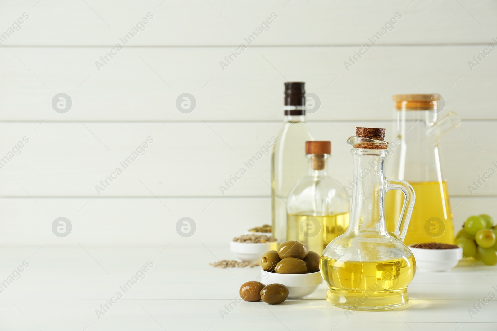 Photo of Vegetable fats. Different cooking oils in bottles and ingredients on white wooden table, space for text