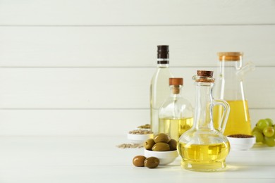 Vegetable fats. Different cooking oils in bottles and ingredients on white wooden table, space for text