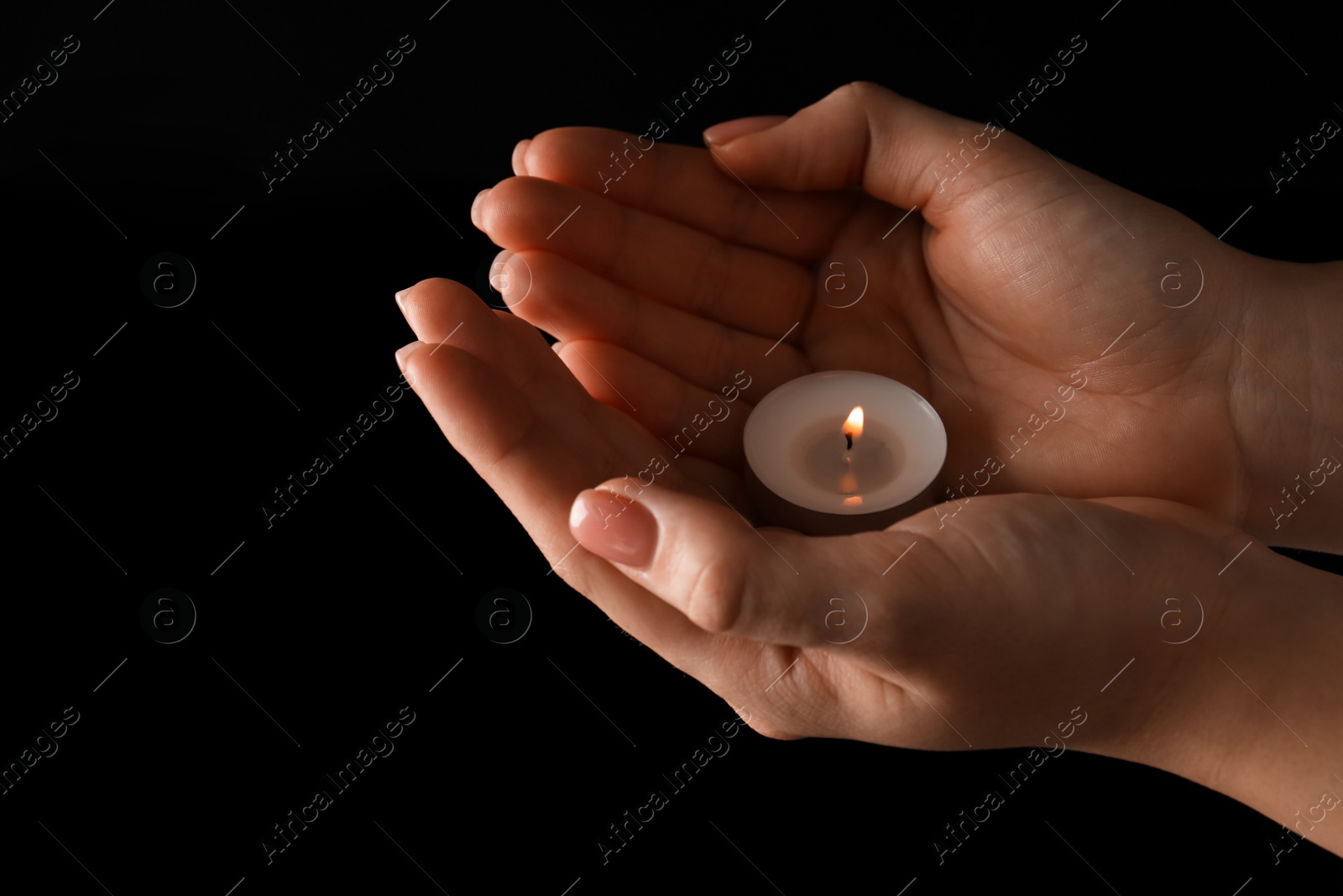 Photo of Woman holding burning candle in hands on black background, closeup. Space for text