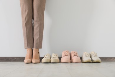 Photo of Businesswoman in high heel shoes near comfortable sneakers indoors, closeup