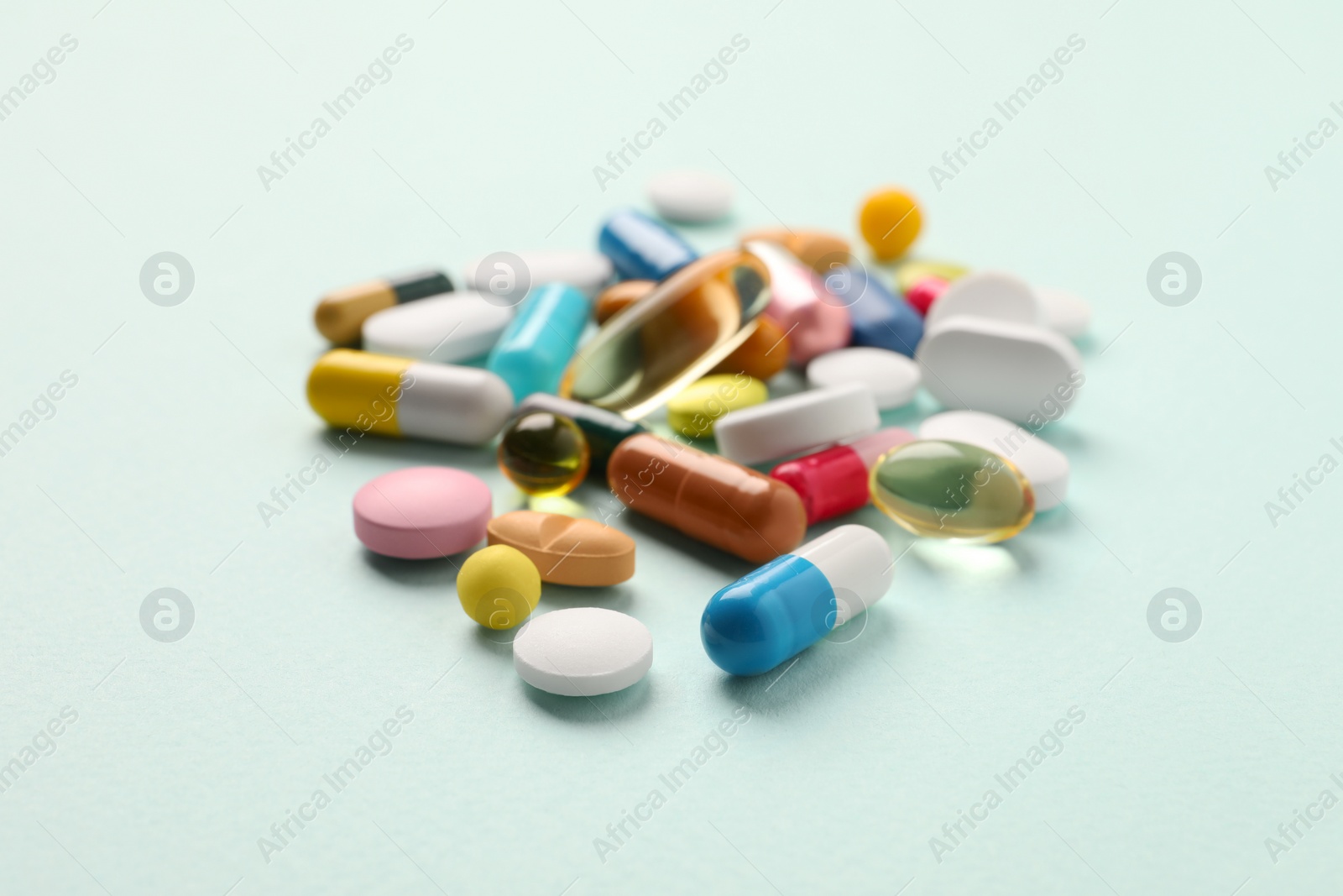 Photo of Pile of different pills on mint background, selective focus