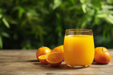 Photo of Glass of fresh tangerine juice and fruits on wooden table. Space for text