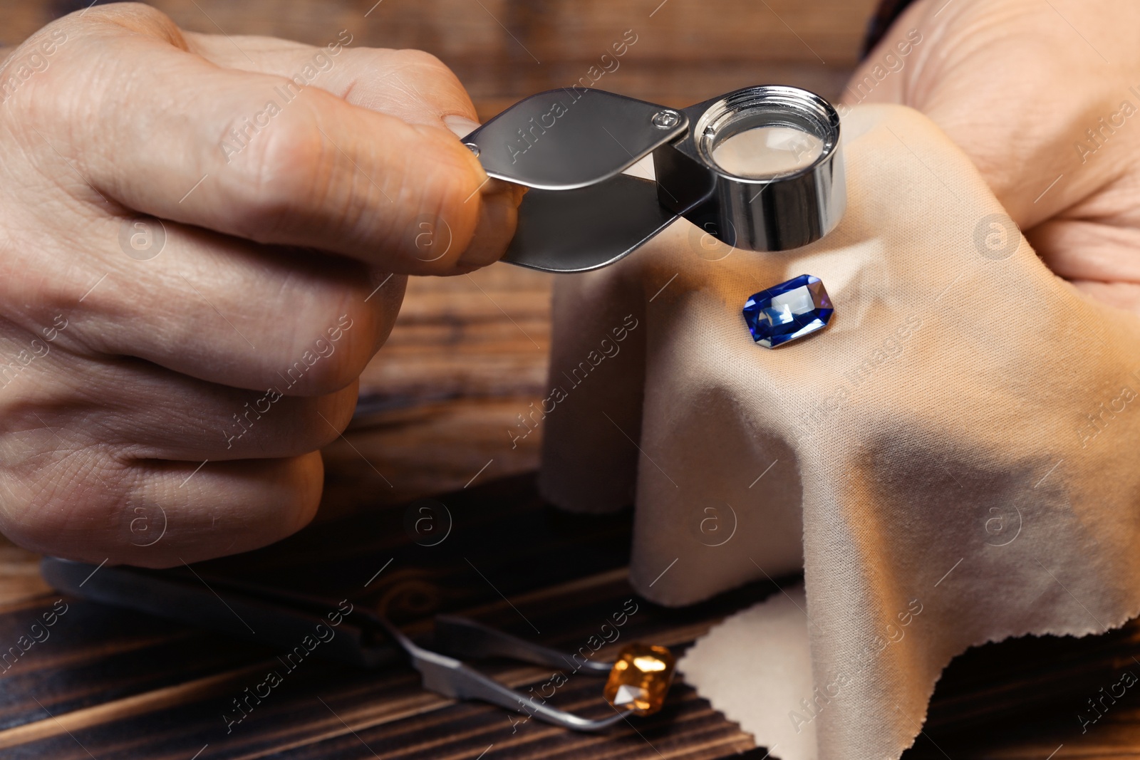 Photo of Professional jeweler working with gemstone at wooden table, closeup