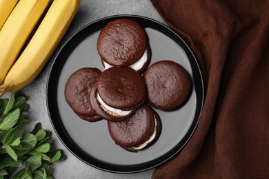 Photo of Tasty sweet choco pies, bananas and mint on brown table, flat lay