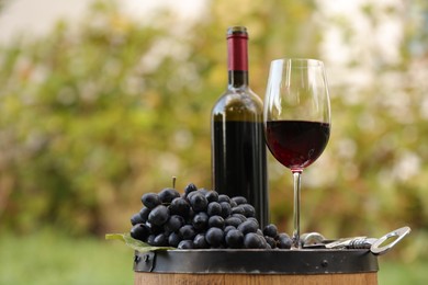 Delicious wine and ripe grapes on wooden barrel outdoors, space for text