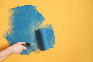 Photo of Man painting yellow wall with blue dye, closeup