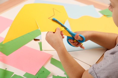 Photo of Little girl cutting color paper with scissors at table, closeup