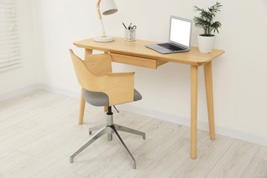 Stylish office interior with comfortable chair, desk, laptop and lamp