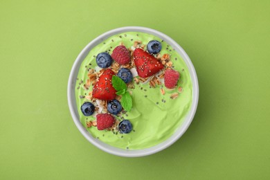 Photo of Tasty matcha smoothie bowl served with berries and oatmeal on green background, top view. Healthy breakfast