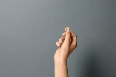 Photo of Young woman holding coin on grey background, closeup. Space for text