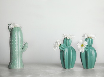 Photo of Trendy cactus shaped vases with flowers on table against light wall. Creative decor