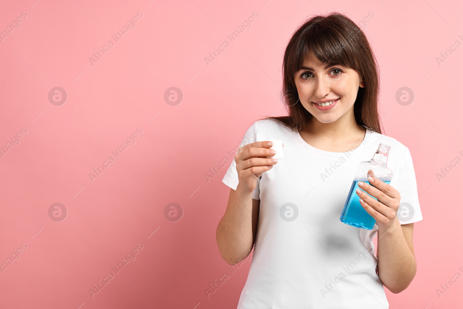 Photo of Young woman with mouthwash on pink background, space for text