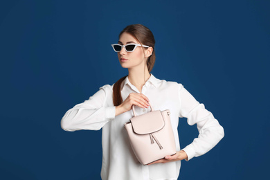 Beautiful young woman in sunglasses with stylish bag on blue background