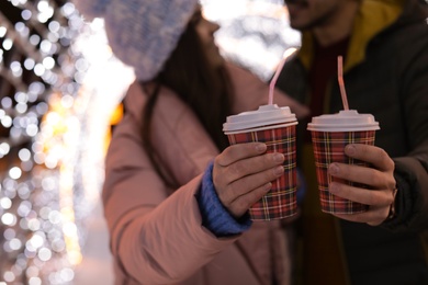 Photo of Young couple with cups of mulled wine at winter fair, closeup