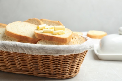 Slices of tasty fresh bread with butter in wicker basket on light marble table