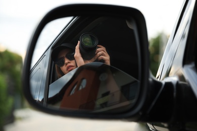 Photo of Private detective with camera spying from auto, view through car side mirror