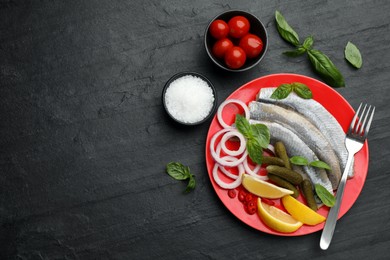 Salted herring fillets served with onion rings, pickles, basil, chili pepper and lemon on black table, flat lay. Space for text
