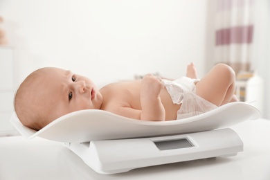 Photo of Cute little baby lying on scales in light room