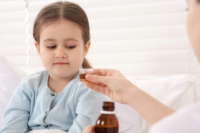 Photo of Mother giving cough syrup to her daughter in bedroom