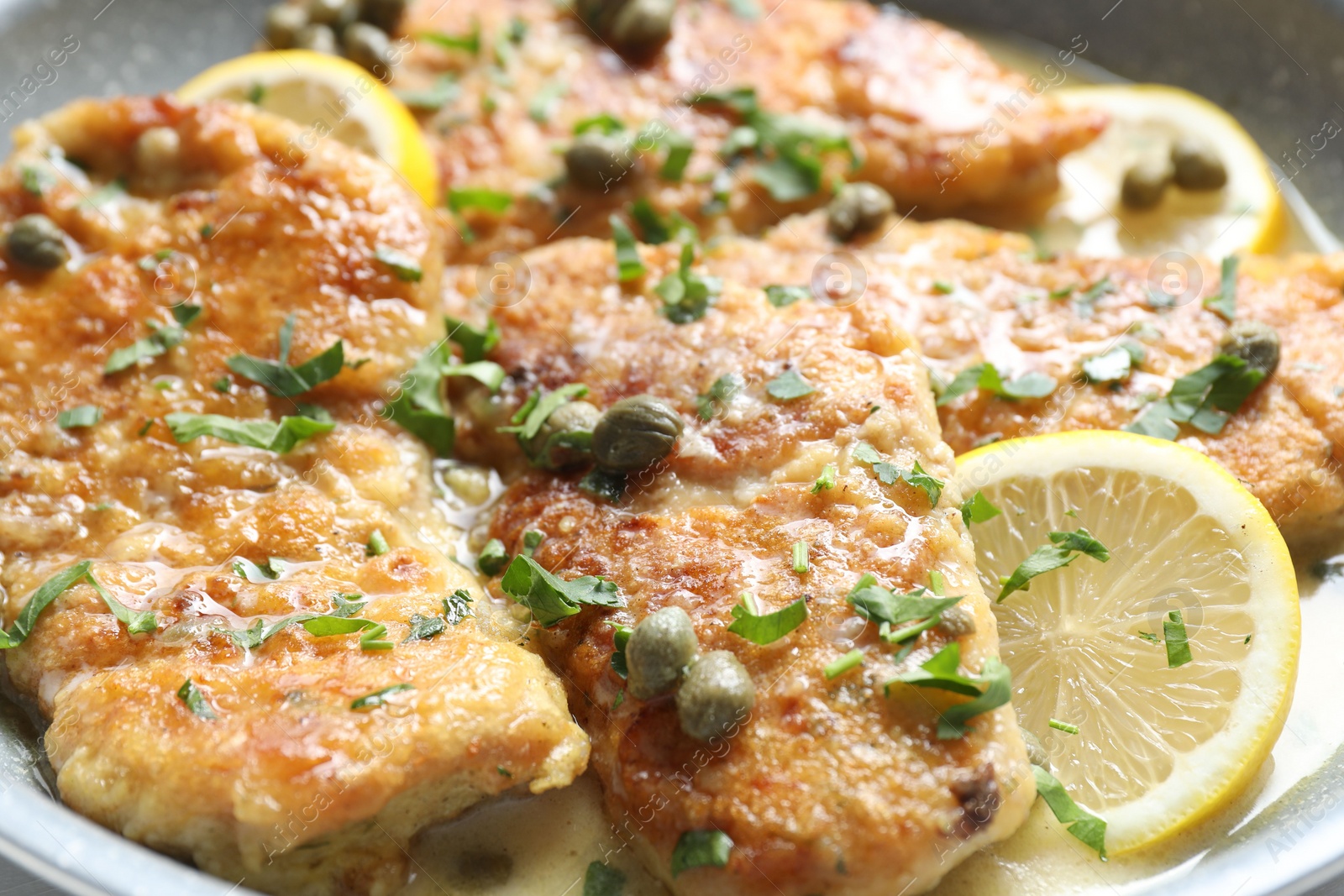 Photo of Delicious chicken piccata with herbs and lemons in pan, closeup