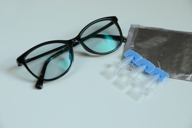 Photo of Single dose eye drops and glasses on white table, closeup