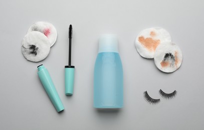 Photo of Dirty cotton pads, eyelashes, mascara and makeup removal product on light grey background, flat lay