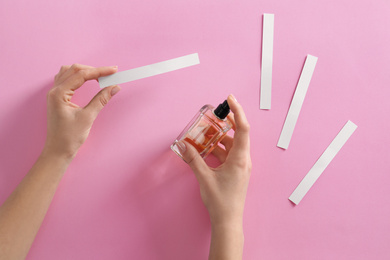 Woman with bottle of perfume and blotters on pink background, top view