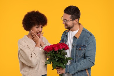 Photo of International dating. Handsome man presenting roses to his beloved woman on orange background